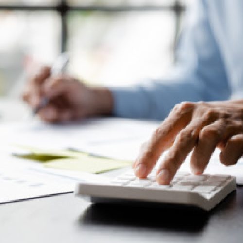 The businesswoman is using a white calculator to check company financial information, she is checking company financial information from the documents provided by the finance department.
